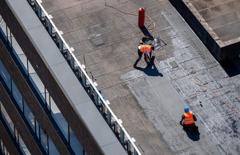 wo roofers in safety vests sealing a commercial roof