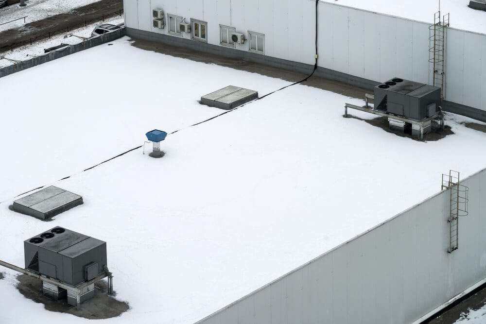 A commercial warehouse roof with HVAC equipment covered in snow.